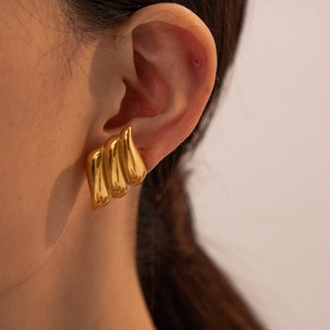 Golden wavy textured teardrop earrings in stainless steel worn on a model's ear