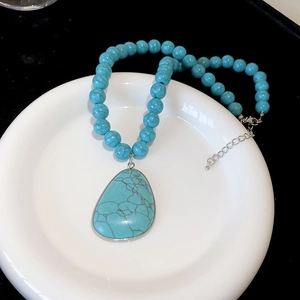 Detail view of Bohemian turquoise-style beaded necklace with teardrop pendant on ceramic plate