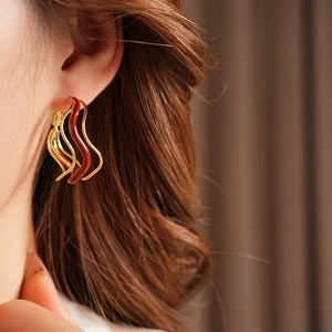 Close-up of golden wavy layered earrings with red enamel on a model side profile