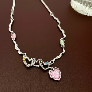 Détail d'une chaîne argentée ondulée avec pendentif cœur rose et pierres de zircon colorées