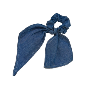 Denim blue bow scrunchie with contrast stitching and textured fabric on white background