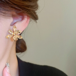 Detailed view of large gold metallic flower earrings with textured petals on a model