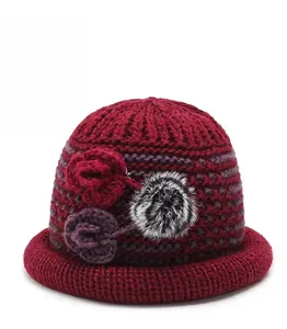Detail of burgundy knitted hat featuring elegant crochet flowers and soft faux fur ball