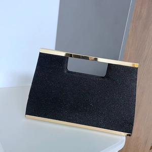 Detail of black glitter evening clutch featuring a gold metal handle and polished bottom trim