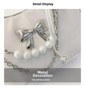 Macro detail of a silver metal bow, faux pearls, and chain on a white pleated bag