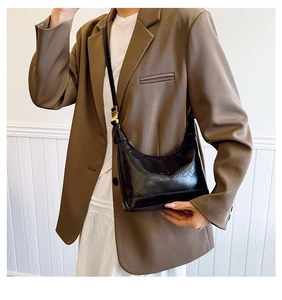 Detail of a chic black glossy crescent bag with embossed text worn with a brown blazer