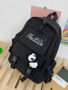 Black canvas backpack with panda pendant and white embroidery on a wooden surface