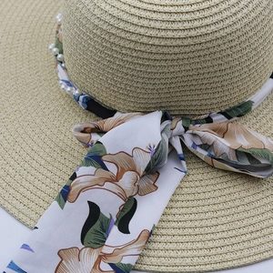 Close-up of bohemian straw sun hat featuring floral ribbon and pearl bead decoration