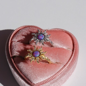 Close-up of gold and silver sun-shaped opal rings in a pink velvet heart-shaped box