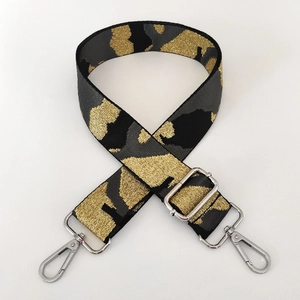 Detail of camouflaged black, grey, and gold woven bag strap with silver metal lobster clasps