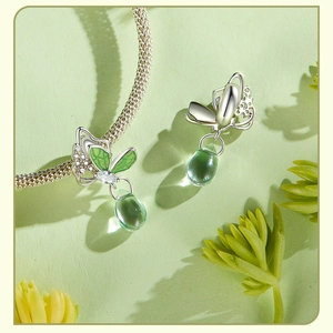 Macro detail of silver butterfly pendant with green water-drop charm and crystal accents