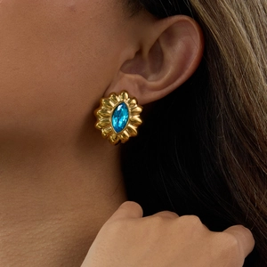 Close-up of gold gear-shaped earring with a large blue marquise-cut zircon gemstone