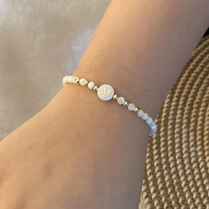 Beaded letter M bracelet with white round beads and gold accents worn on a woman's wrist