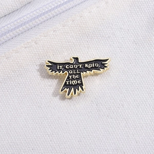 Detail of raven enamel pin with 'IT CAN'T RAIN ALL THE TIME' text and gold metal trim