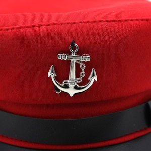 Detail shot of a silver metal anchor badge on a red knitted navy style captain hat