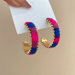 Detail view of colorful knitted yarn wrapped around golden C-shaped hoop earrings