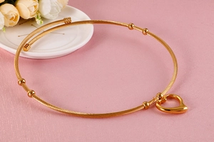 Detail of a golden wire neck torque featuring a hollow heart pendant on a white plate