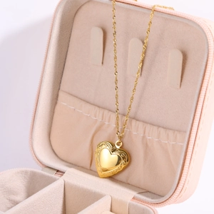 Detailed macro view of a golden heart locket necklace with floral relief in a pink gift box