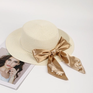 Flat top straw sun hat with elegant pearl trim and a large golden satin bow detail