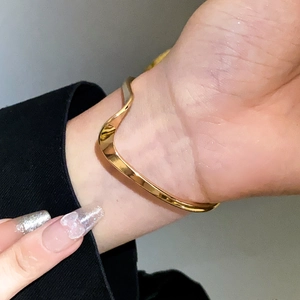 Detail view of wavy gold-tone cuff bracelet with a polished metallic finish on the wrist