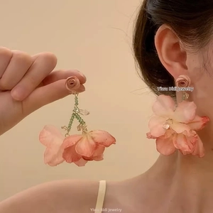 Détail de boucles d'oreilles à fleurs avec pétales roses et perles vertes sur un mannequin