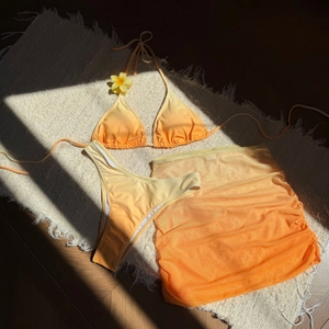 Bikini trois pièces dégradé jaune et orange avec paréo en mesh posé sur un tapis