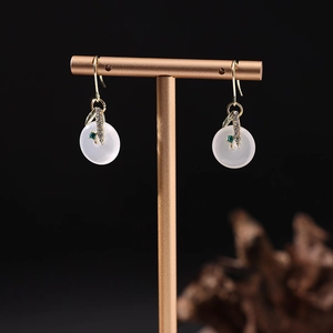Détail de boucles d'oreilles en jade blanc avec gemme verte sur un support doré en T