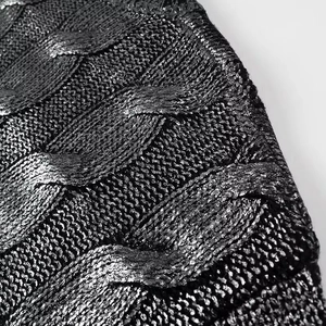 Détail de la texture en maille torsadée noire du pull avec un fini métallique doré