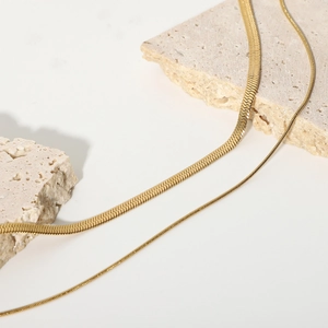 Detail of layered gold snake chain necklace on beige stone props with white background