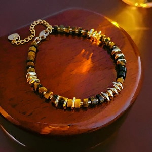 Macro shot of tiger eye beaded bracelet with gold heart charm on dark wood surface