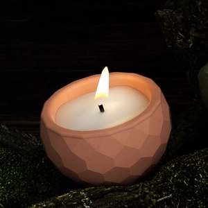 Close-up of a faceted geometric candle jar in clay pink with a bright flickering flame