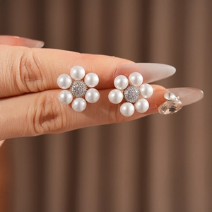 Close-up of pearl flower earrings with zircon center held by fingers for detail