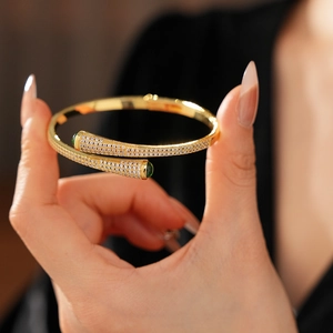 Macro detail of gold plated open bangle with pavé zircons and green gemstone accents