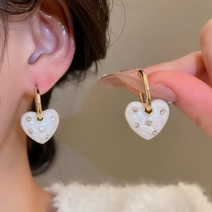 Detail of gold heart earrings with shell texture and diamonds worn by a model