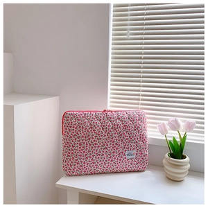 Pink floral quilted laptop sleeve with zipper on desk next to a tulip flower pot