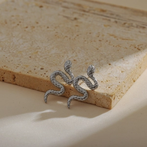 Silver snake-shaped stud earrings with scale texture on a light stone surface