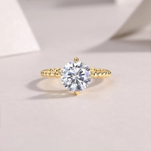 Close-up of moissanite ring with beaded 18K gold band on a minimalist background