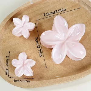 Pink frangipani flower hair clips in three sizes on a wooden tray for elegant styling