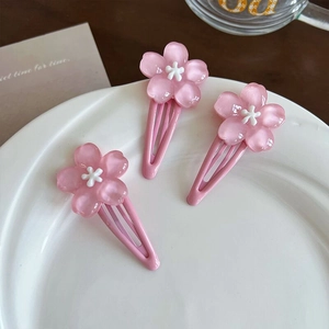 Three sweet pink cherry blossom hair clips with resin petals on a white ceramic plate