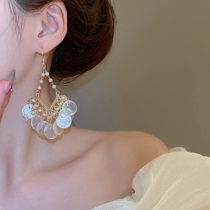 Close-up of pearl drop earrings with round shell charms and gold filigree on a model