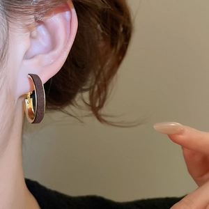 Detail of a vintage-style gold hoop earring with dark brown texture worn by a model
