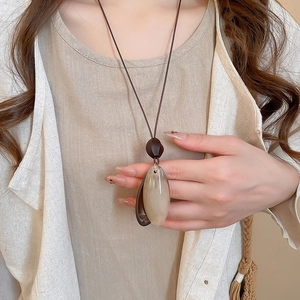Detail of oval resin and wood pendant on long brown cord necklace worn by model