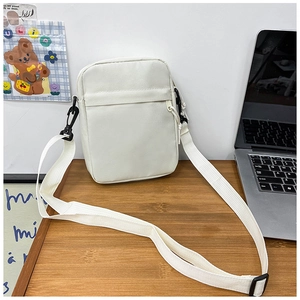 Close-up of minimalist off-white canvas crossbody bag with adjustable strap on wooden table