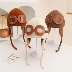 Nahaufnahme von drei Kinder-Strickmützen im Fliegerstil mit Brille und Ohrenschutz