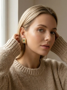 Detail of square gold evil eye stud earrings with green zircon on a female model