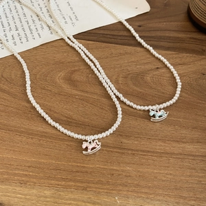 Close-up of pearl necklaces with pink and blue rocking horse pendants on wooden desk