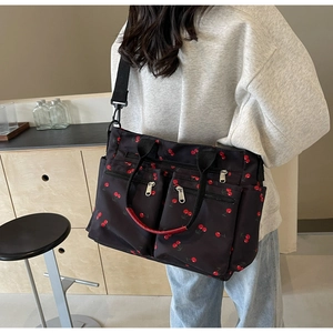 Close-up of black tote bag with red cherry print featuring multiple zipper pockets and straps