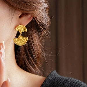 Gros plan de boucles d'oreilles vintage dorées en forme d'éventail sur un mannequin