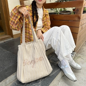 Detail of striped canvas tote with Bonjour embroidery carried by model on stone steps