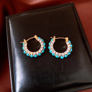 Detail of gold-plated hoop earrings with turquoise and white zircon on black leather box